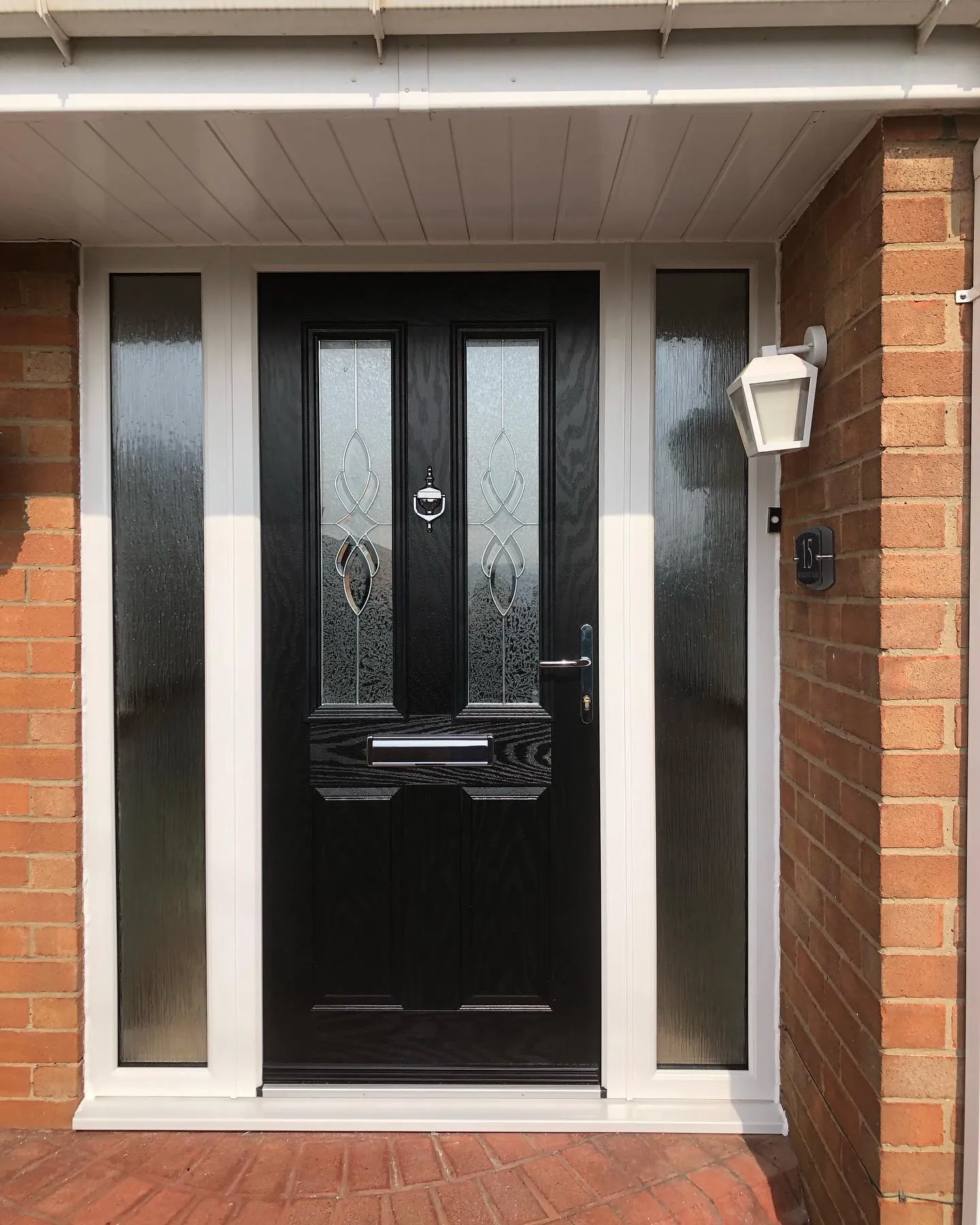 A black front door with two sidelights on a brick house.
